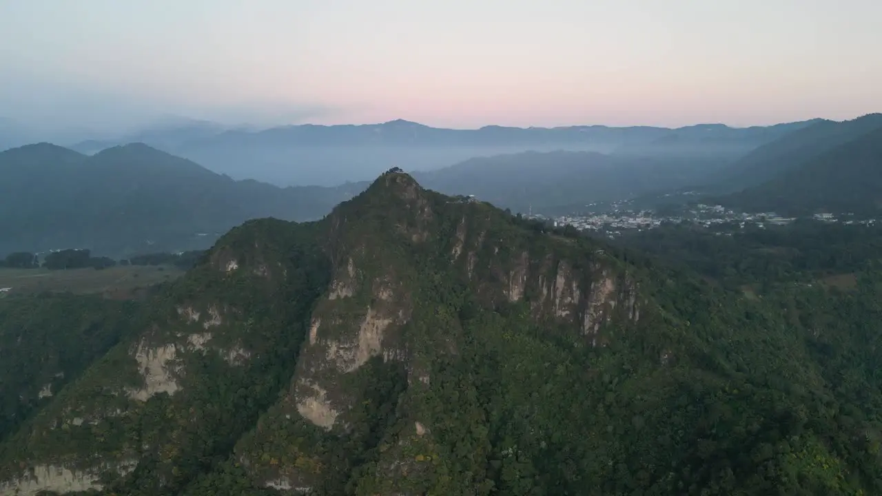 Drone view in Guatemala flying in front of a green mountain surrounded by volcanos on a cloudy day in Atitlan