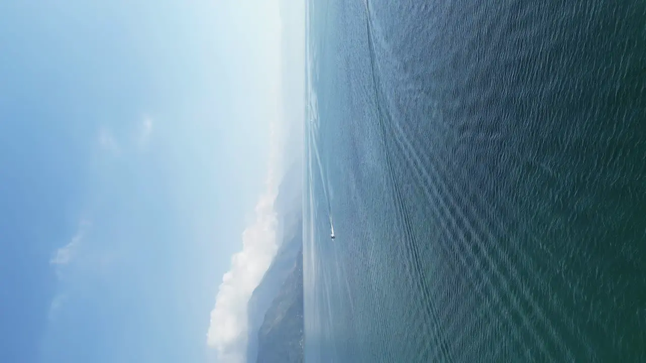 Drone portrait view in Guatemala flying over a blue lake surrounded by green mountains and volcanos on a cloudy day in Atitlan