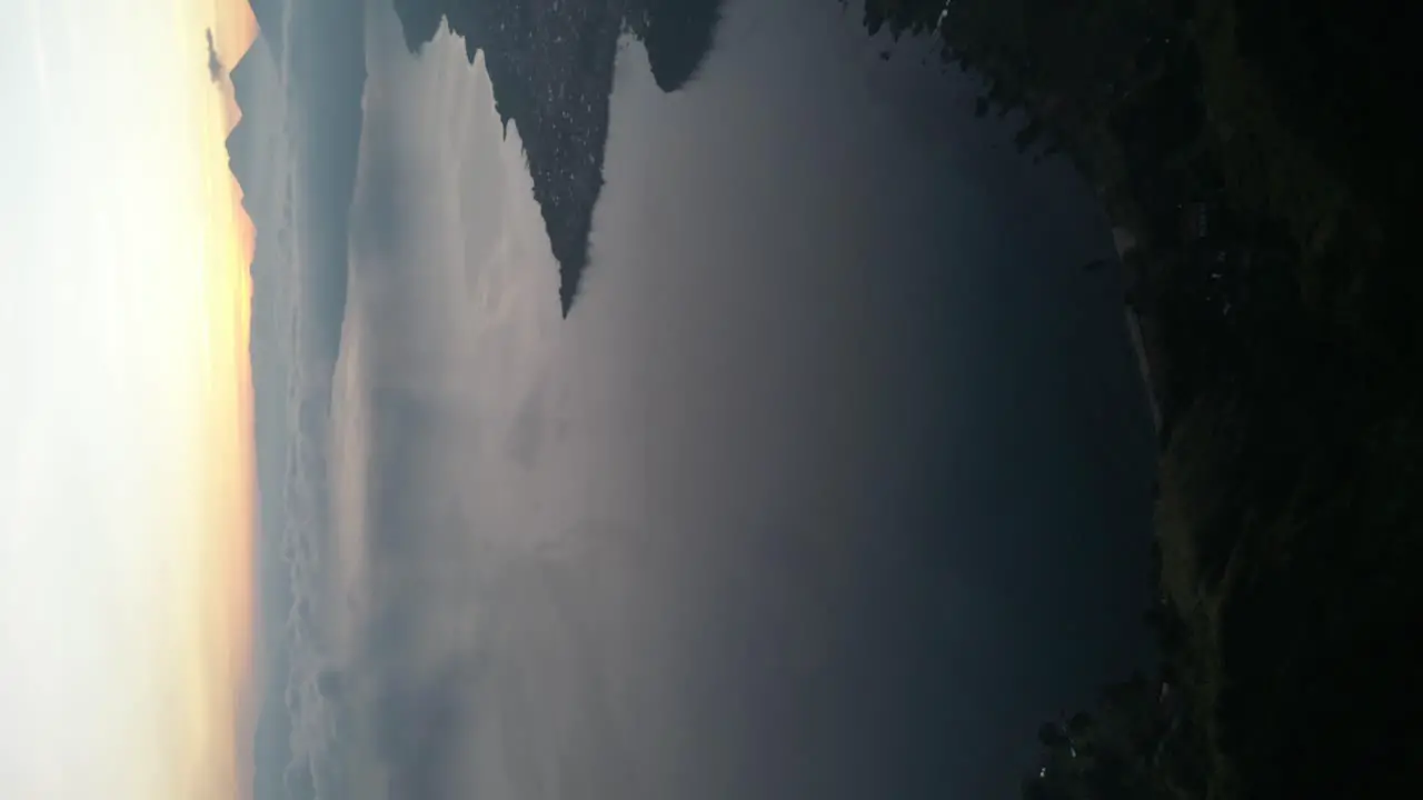 Drone portrait view in Guatemala flying over a blue lake surrounded by green mountains at sunrise on a cloudy day in Atitlan