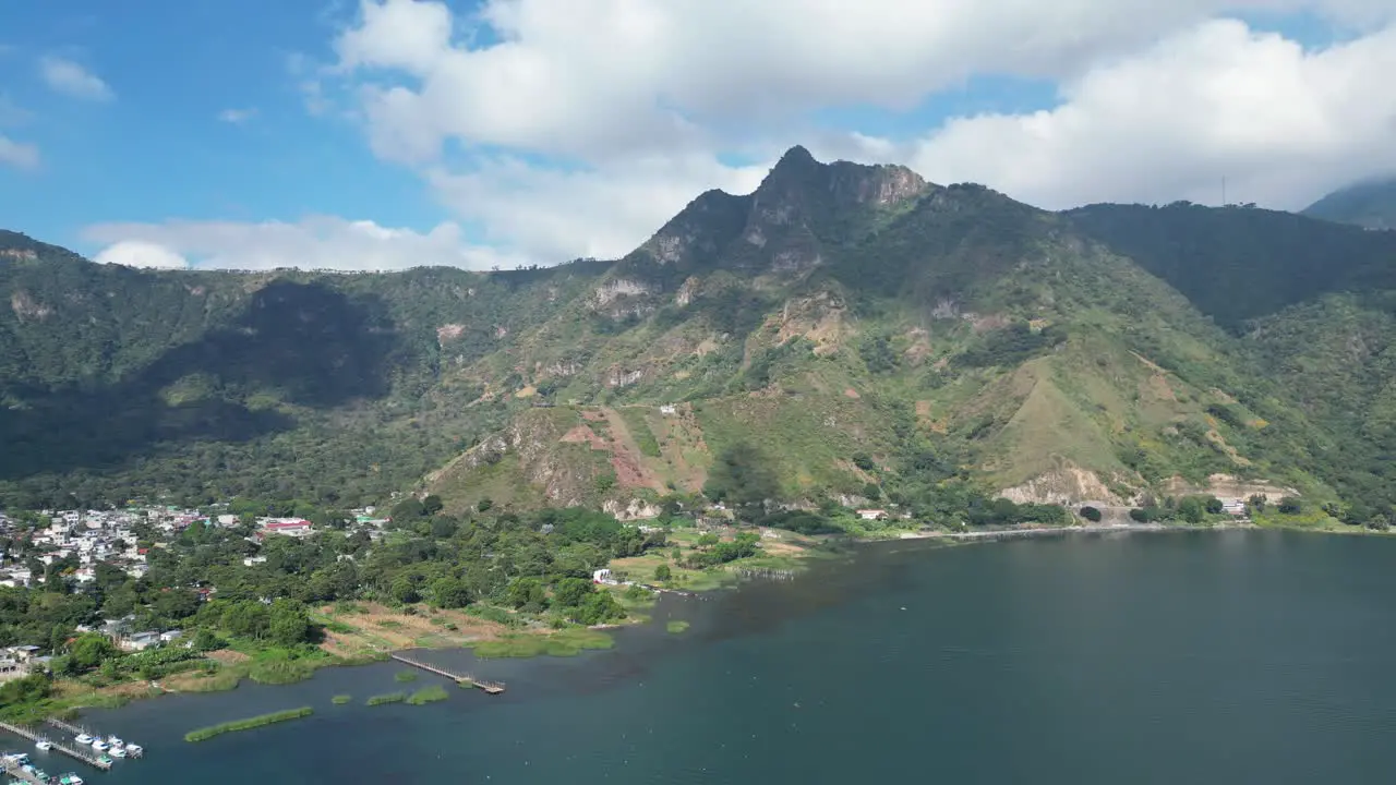 Drone view in Guatemala flying over a blue lake surrounded by green mountains and volcanos on a sunny day in Atitlan