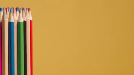 Studio Shot Of Rotating Multi-Coloured Pencils Against Yellow Background 