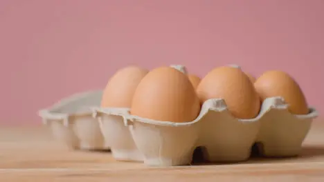 Studio Shot Of Person Opening Cardboard Box Containing Brown Eggs Against Pink Background