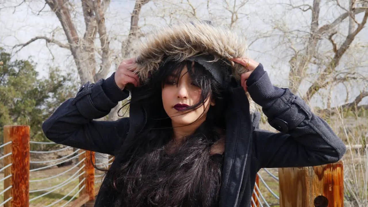 An attractive young woman putting on her jacket hood and smiling during stormy bad weather SLOW MOTION