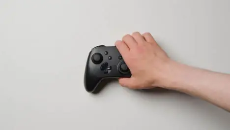 Overhead Studio Shot Of Hand Reaching In To Pick Up Video Game Controller 1