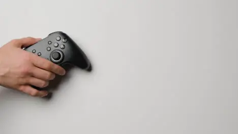 Overhead Studio Shot Of Hand Reaching In To Pick Up Video Game Controller