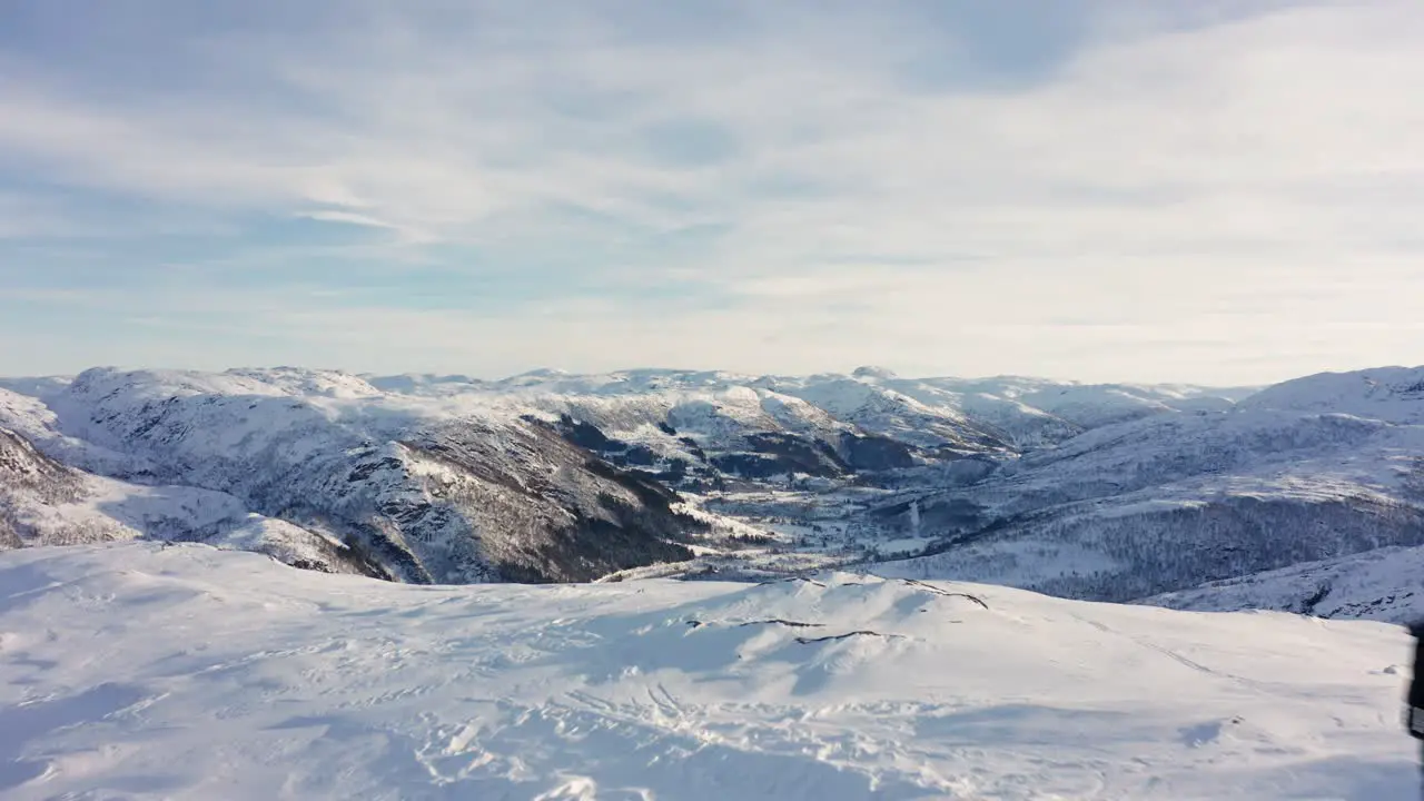 Aerial shot flying over man standing on mountain peak surrounded by snowy landscape