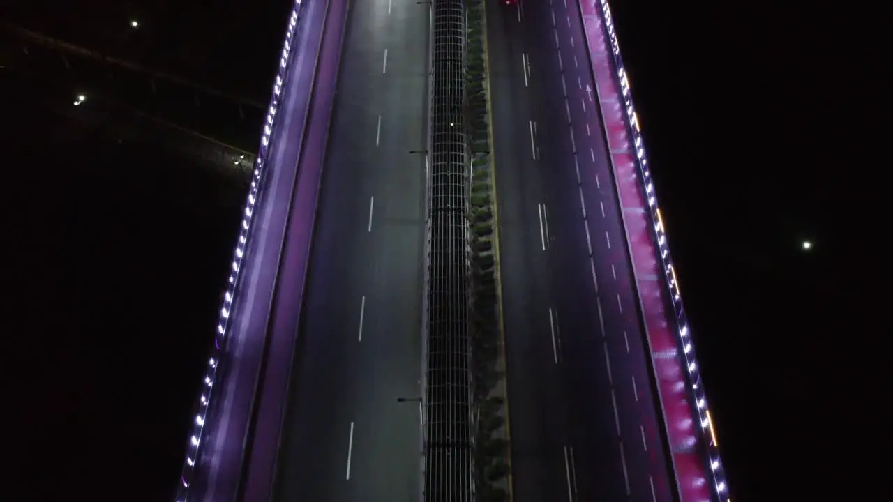 Drone topdown video of a bridge at night lit by purple LED lights