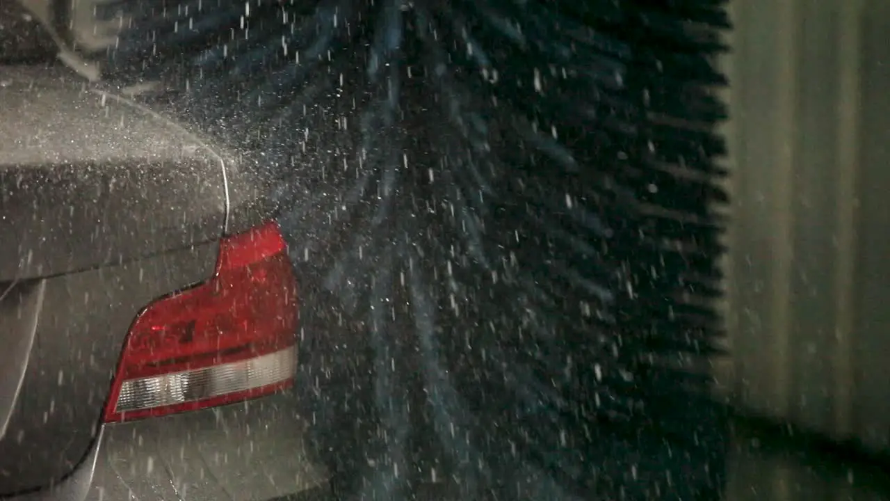 A handheld camera captures the silver car's rear end under the caress of a car wash brush