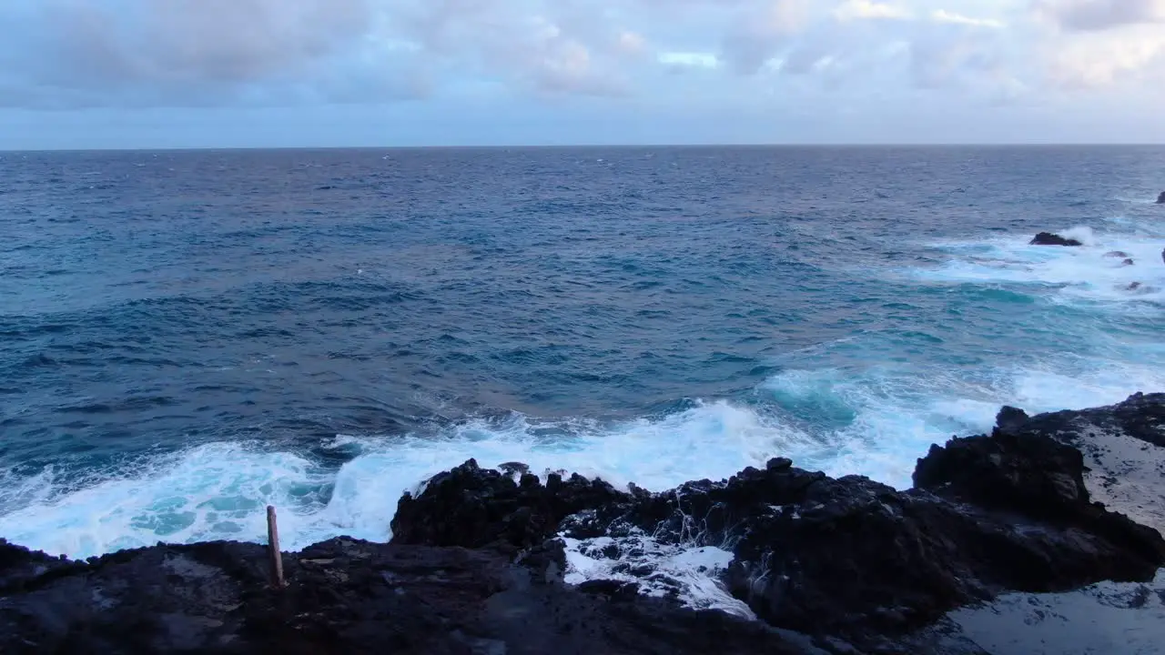 Hawaiian blowhole active on a cloudy day as rough waves crash on the reef cliff