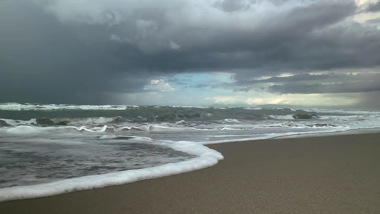 Sea waves run along the sandy shore storm clouds in the background