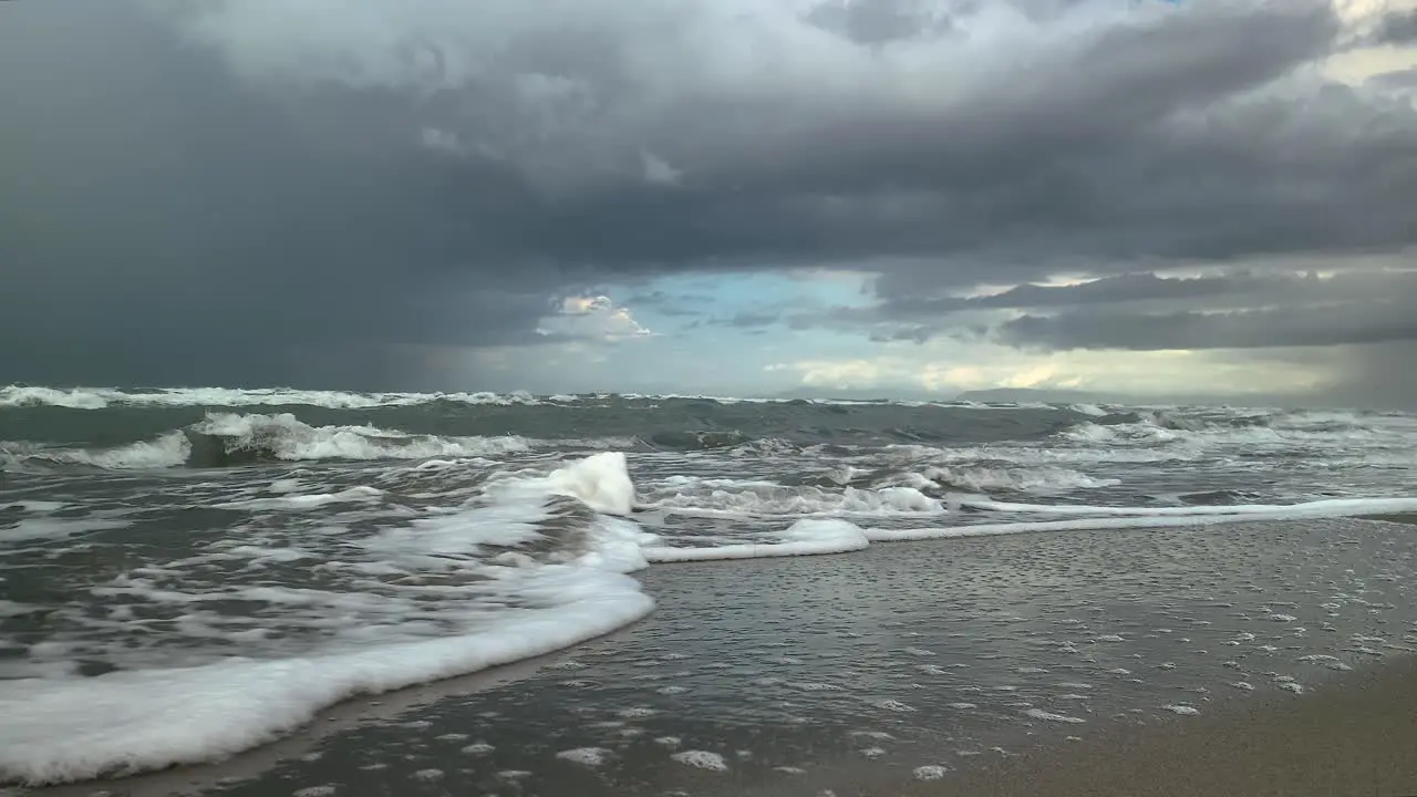 Sea waves run over the sandy shore storm clouds in the background