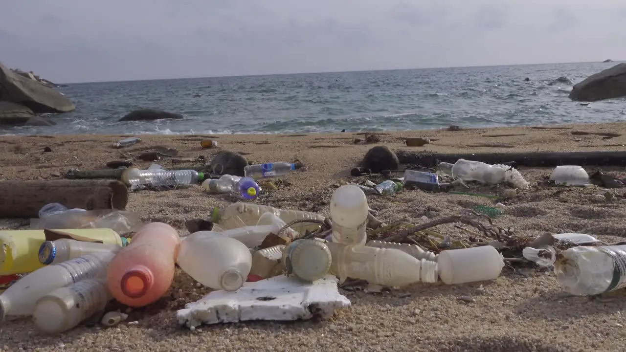 Lots of plastic bottles littered in beachfront near-continuous rushing wave static shot 4k