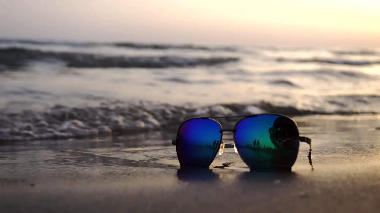 Sea waves washing over sunglasses against a backdrop of a setting sun