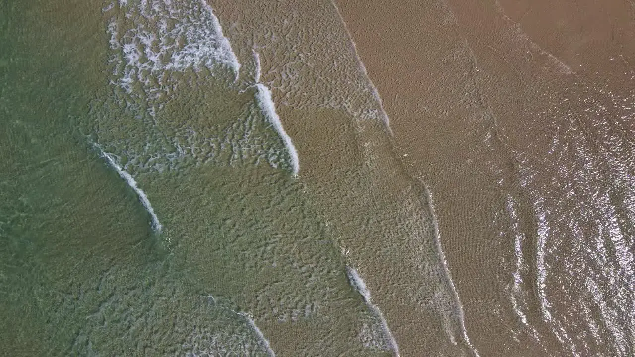 small waves slowly break on a beach aerial view