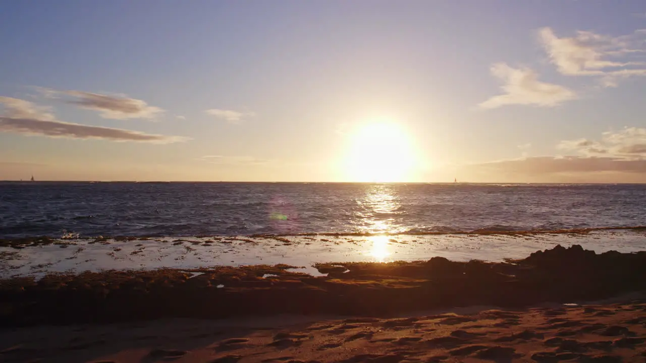 a brilliant white light sun sets behind the Pacific Ocean from a sandy beach on Diamond Head Hawaii Oahu as the Pacific waves roll onto the sandy beach