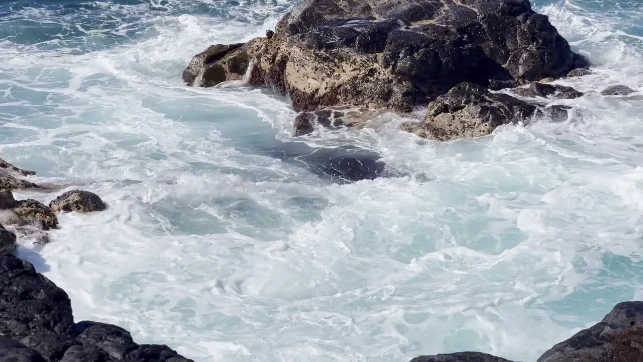 Cinematic close-up shot of ocean swell filling an ancient lava rock tide pool near Queen's Bath on the northern coast of Kaua'i in Hawai'i