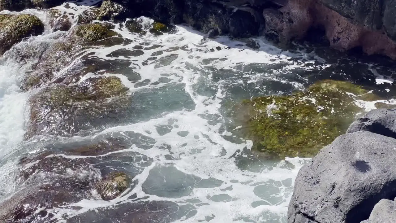 Cinematic close-up panning shot of a tide pool with swirling ocean swell near Queen's Bath on the north coast of Kaua'i Hawai'i