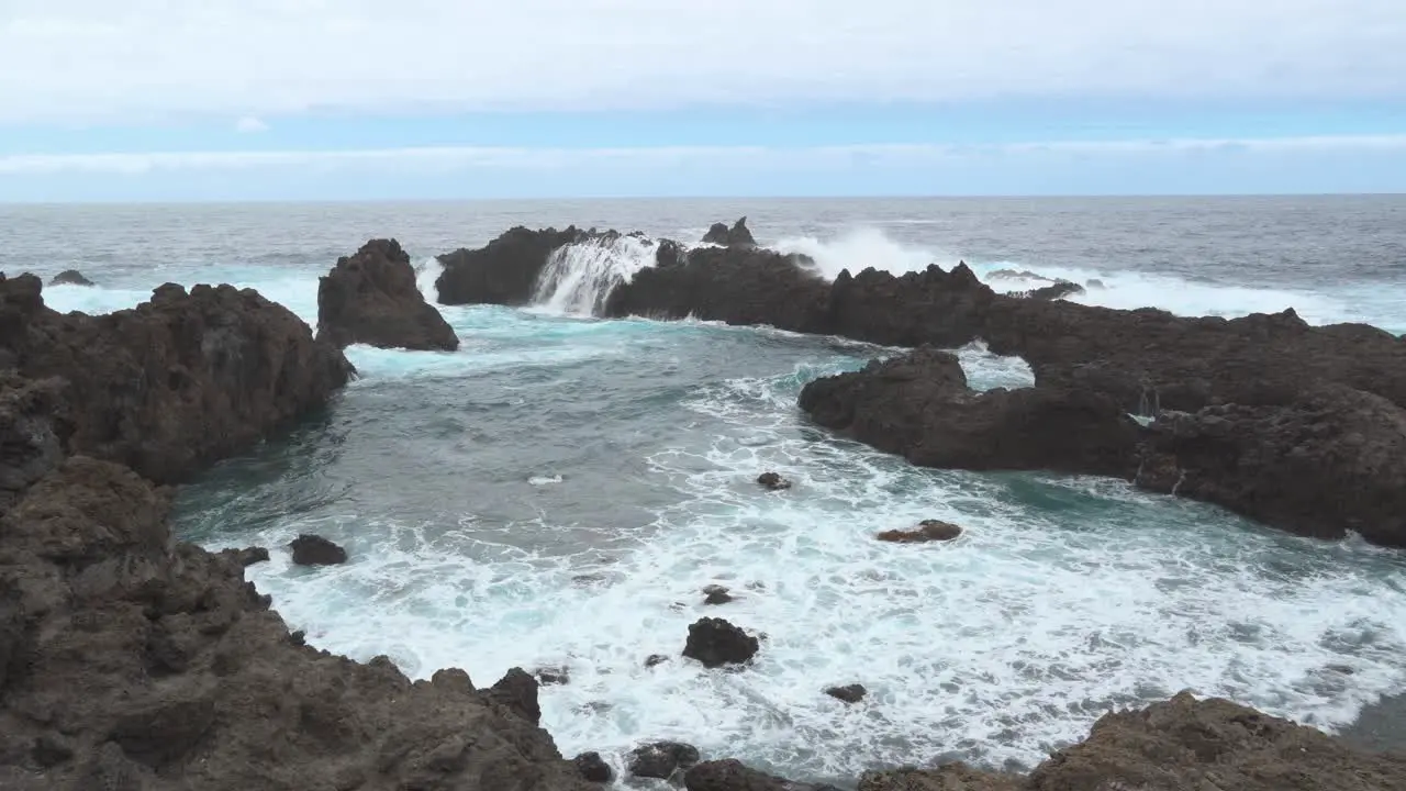 Ocean Waves Hitting The Black Rocky Shoreline Sea Foam Blue Sky White Clouds