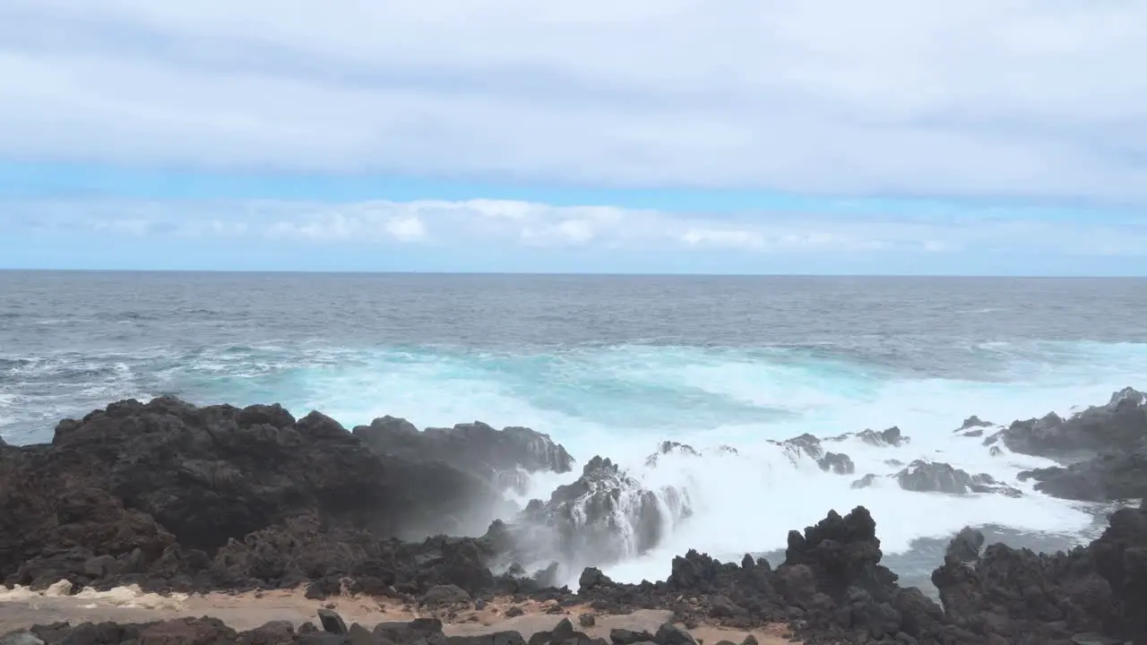 Ocean Waves Crashing Violently Against The Black Rocks On The Shore White Foam Forming Blue Sky Power Of Nature