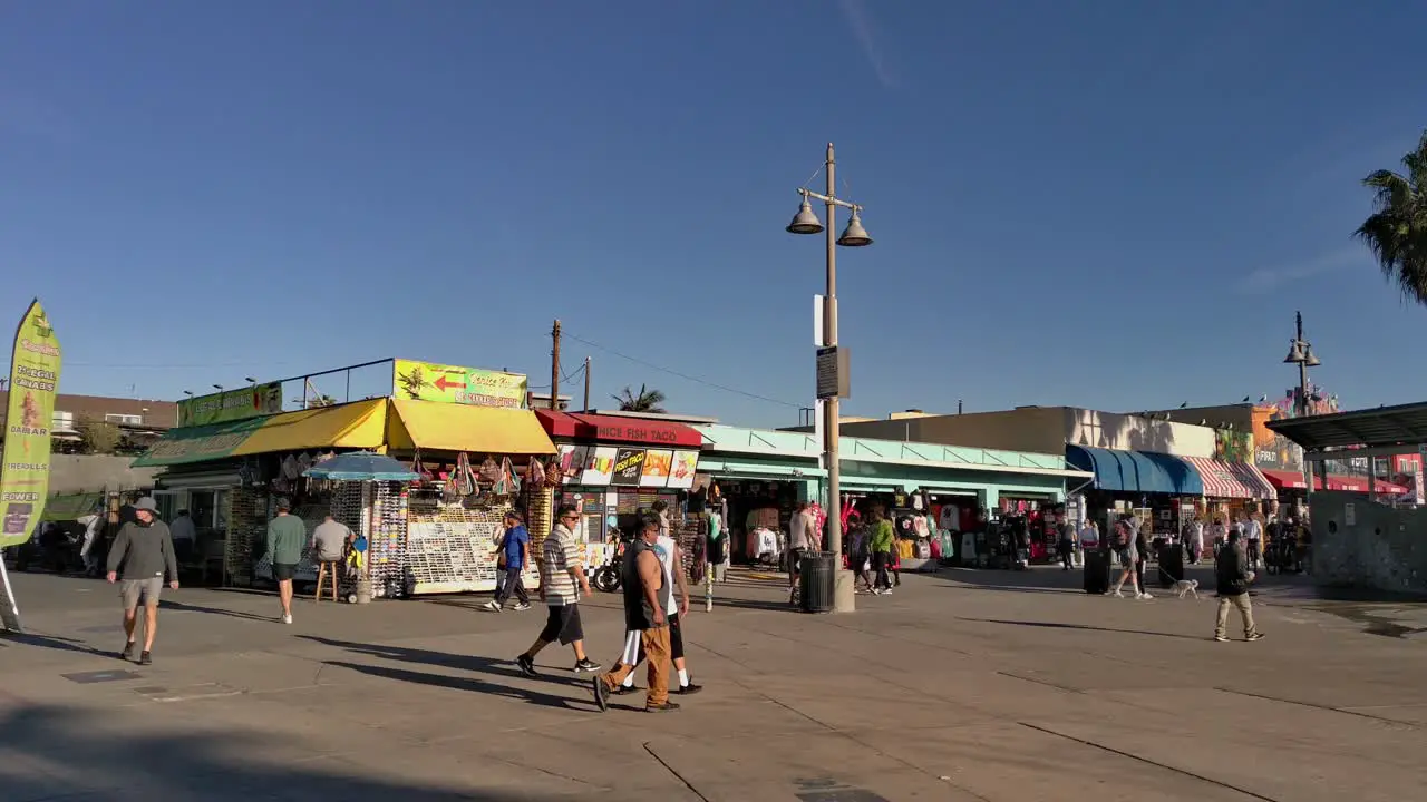 People Leisurely Walking Biking Rollerblading And Skateboarding At Ocean Front Walk Next To Gift Shops And Food Stalls Near Venice Beach In Los Angeles California USA