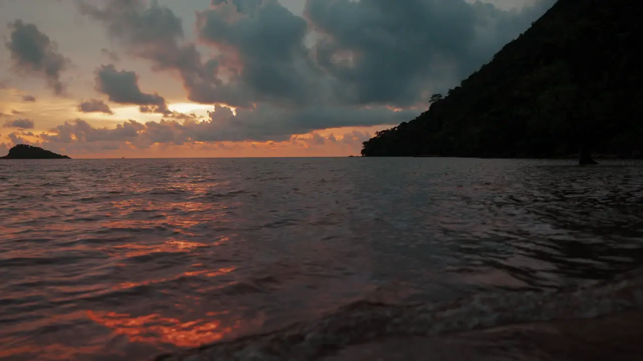 Gentle ocean waves caress the lonely beach in Koh Chang Thailand while the sky is ablaze with the warm hues of a breathtaking sunset – a vivid canvas of yellow orange and red