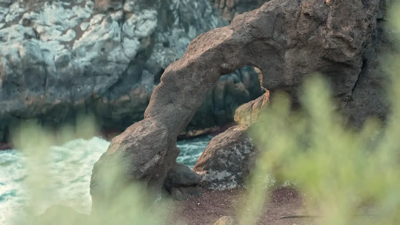 Grass foreground out of focus with small rock arch and slow motion ocean waves crashing on cliffs