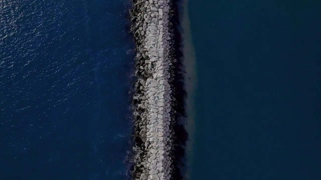 Birdseye view following jetty separating blue ocean water and sand bank