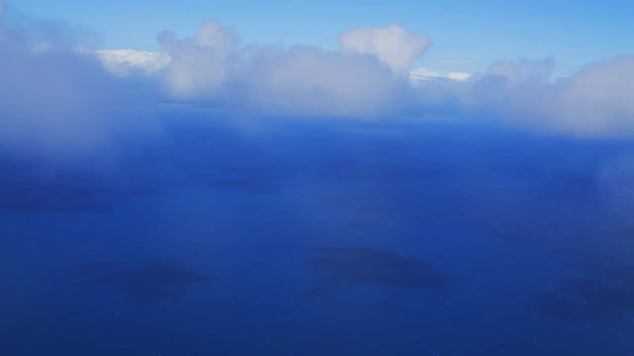 A view from a plane captures the breathtaking sight of going through the clouds above the sea showcasing the beauty of the white fluffy clouds contrasting with the deep blue of the ocean