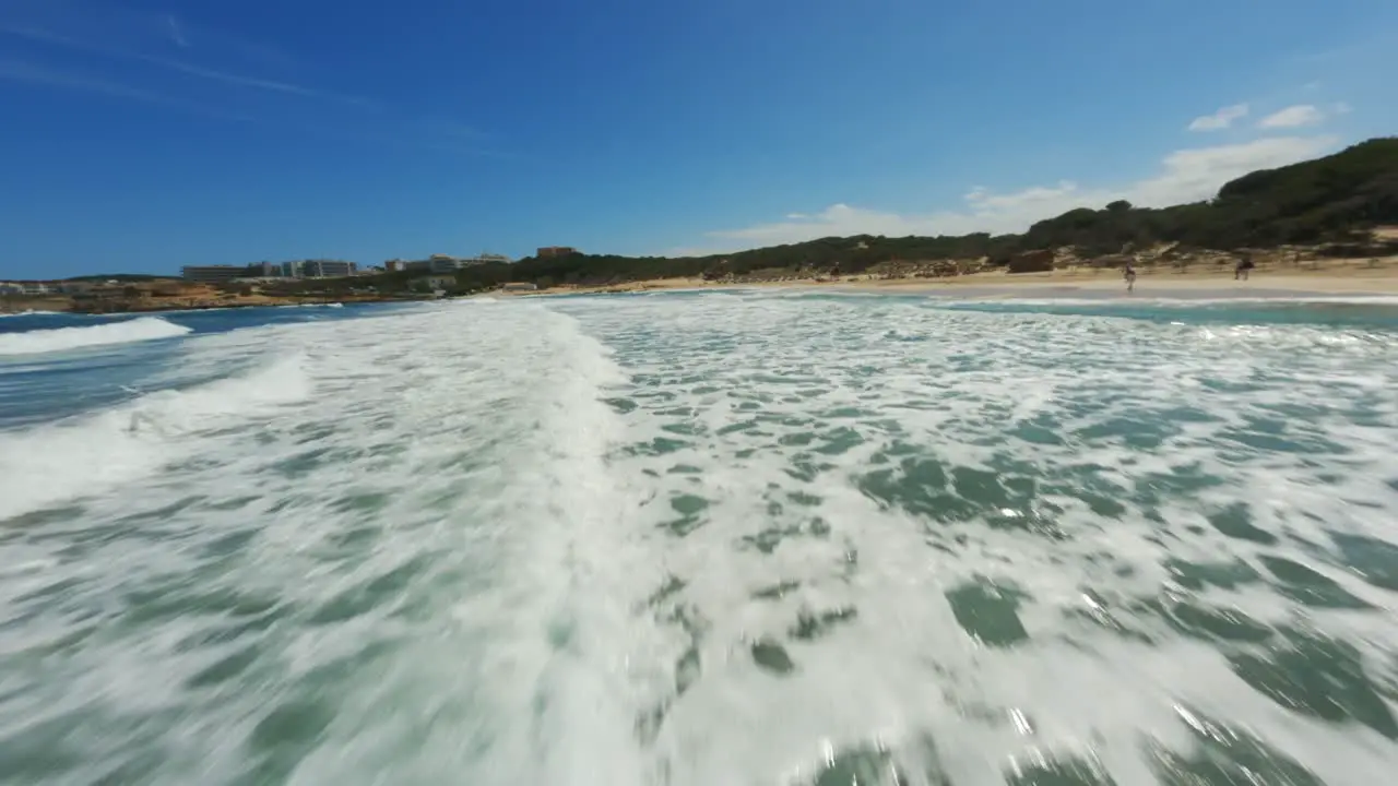 FPV drone riding the clear blue surf on a beautiful amazing beach day with blue skies at high speed