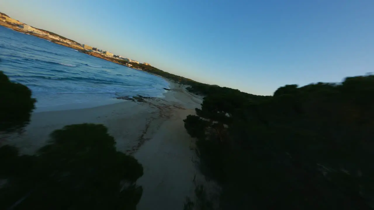 FPV Drone flying close over trees and water during golden hour sunset on beautiful island and beach