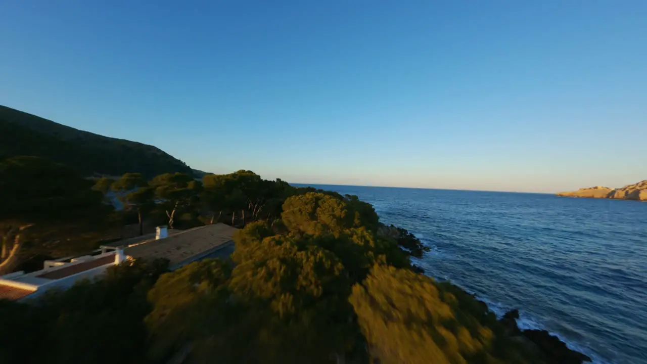 FPV Racing drone flying over beach coast line towards the ocean at golden hour sunset