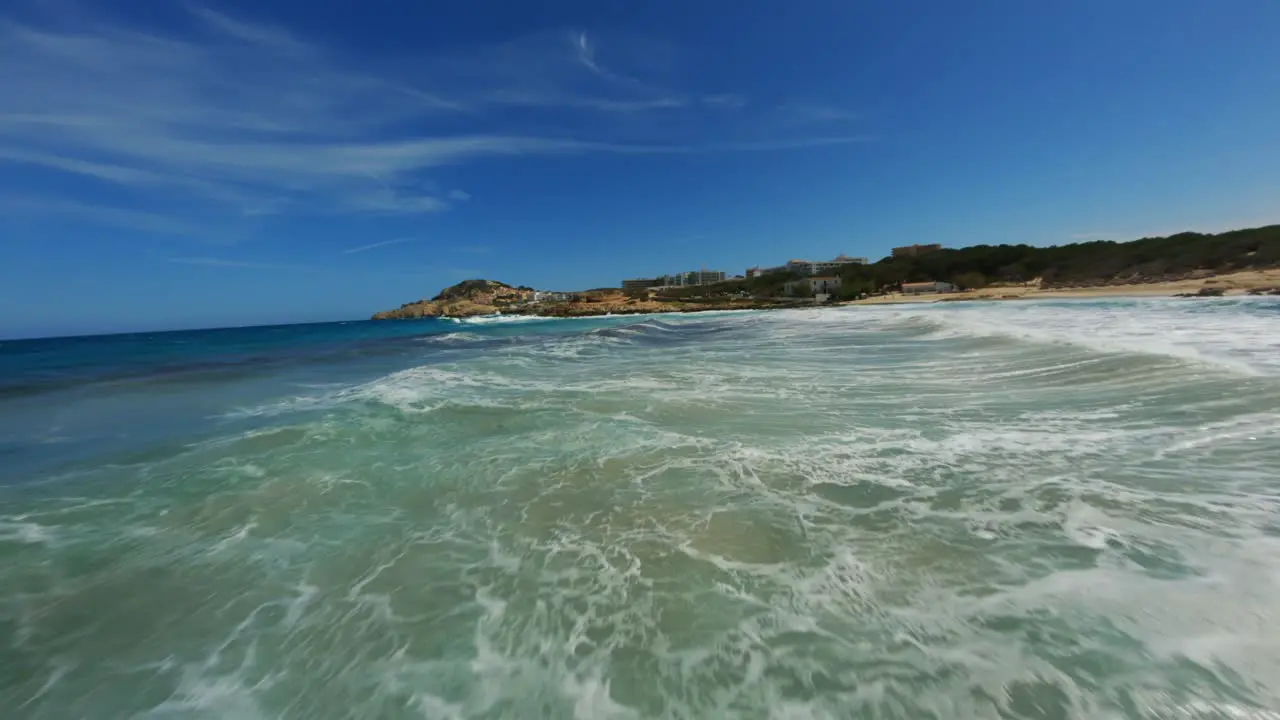 FPV drone closely passing splashing waves and surf on a beautiful day with clear skies and water at high speeds