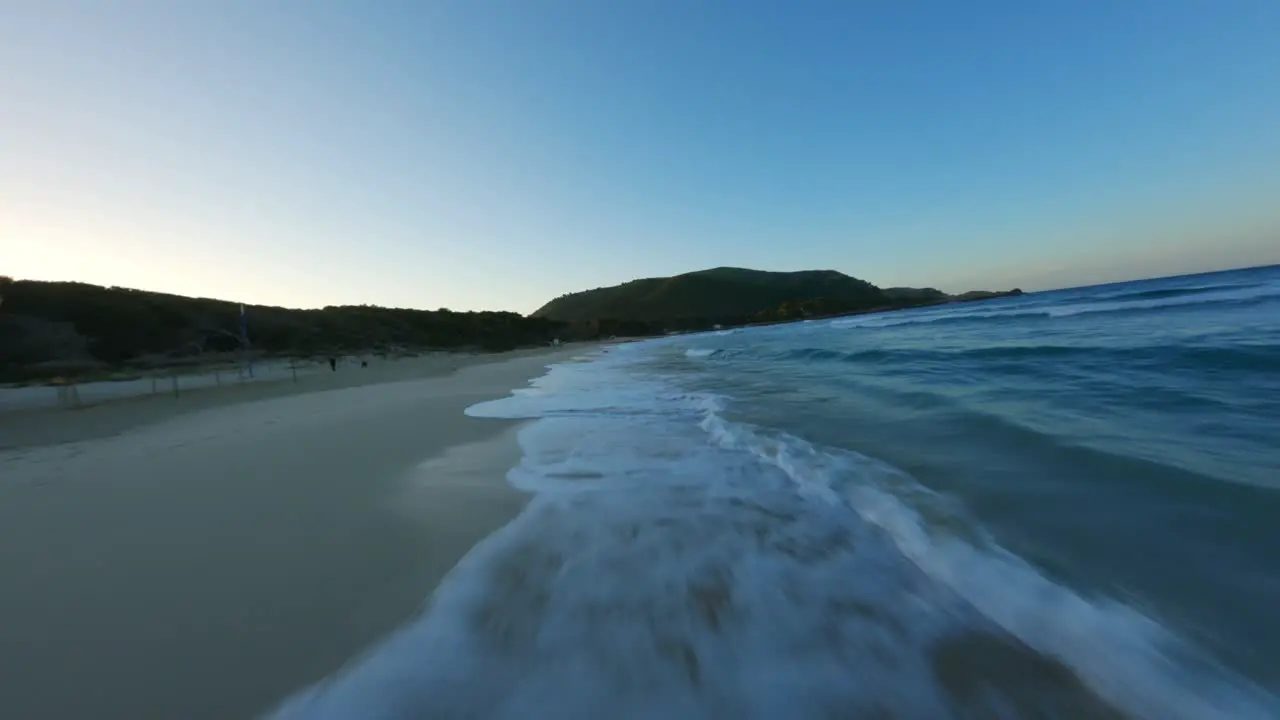 FPV Drone flying over splashing waves at the beach during sunset with seagull crossing the shot