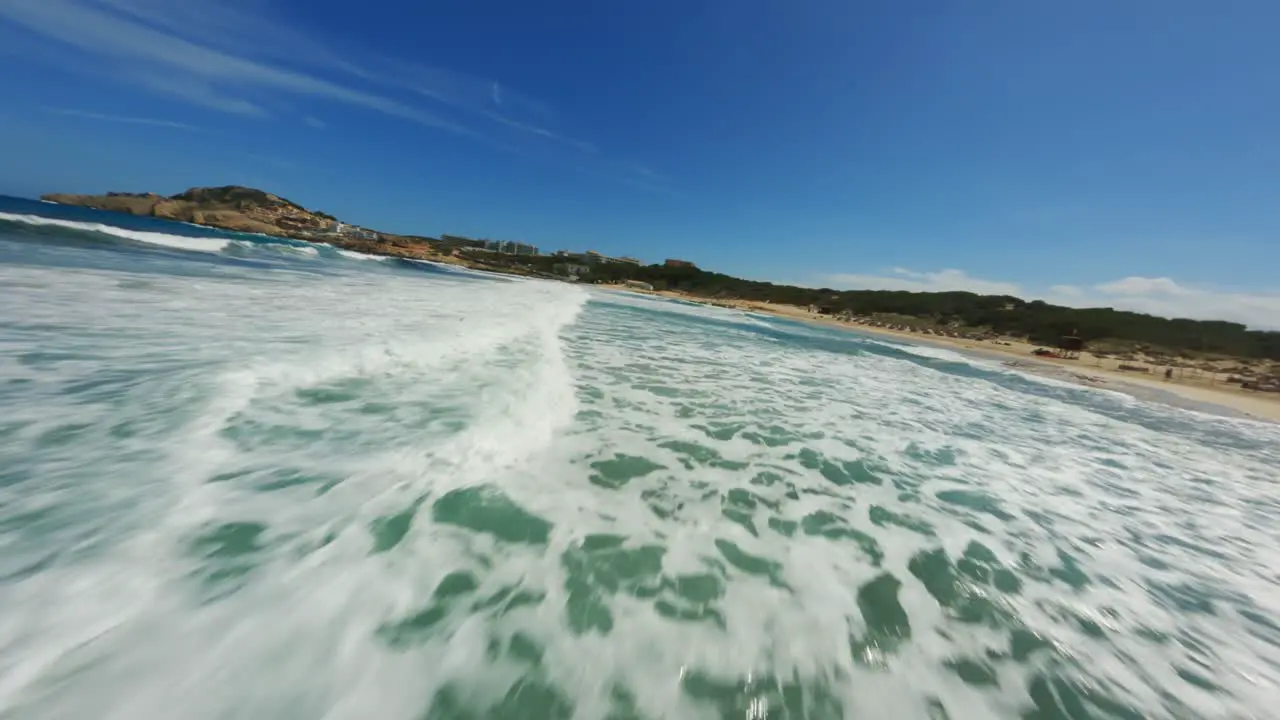 FPV Drone flying closely over splashing and foamy waves and surf with clear blue water and skies at high speeds at the beach