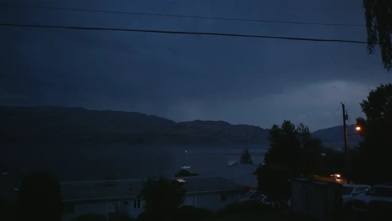 Lightning storm flashes in clouds at night over lake and mountain town Canada