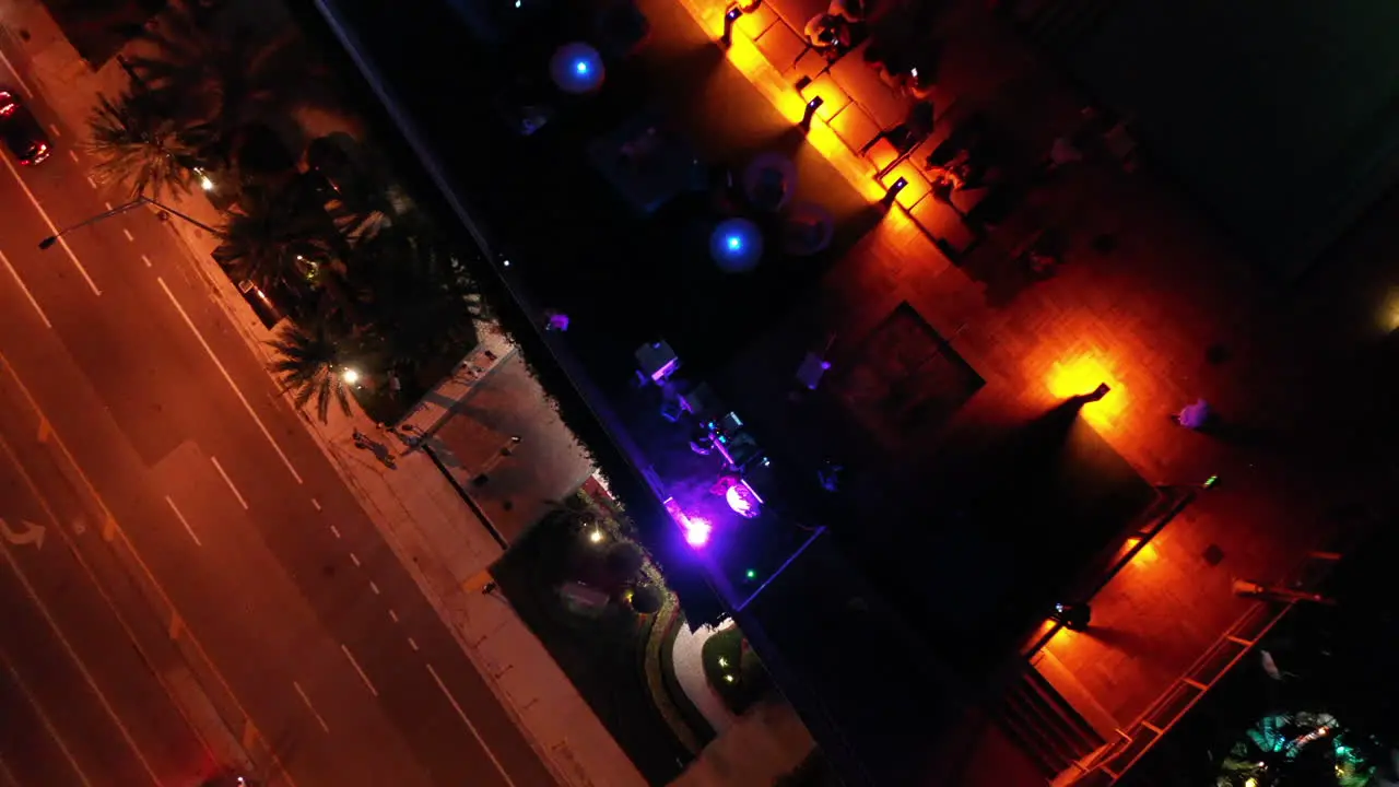 Nighttime Aerial top-down bird's eye pedistal movement of rooftop bar and street with walking people and passing cars