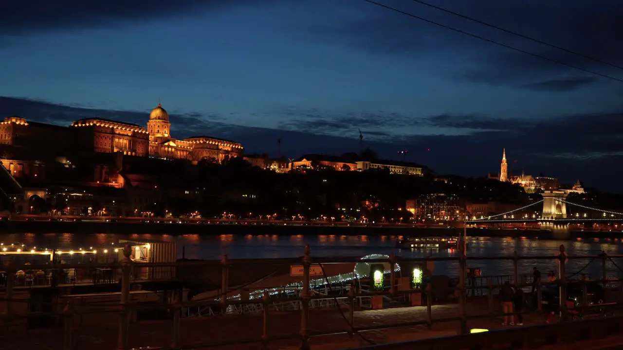 A beautiful evening view of Buda with Castle Hill lit in orange light as riverboats cruise the Danube River