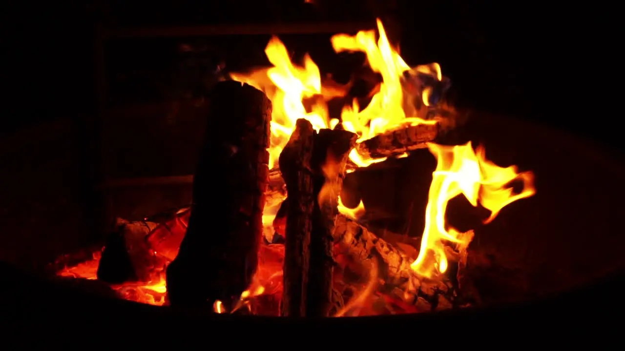 Campfire flames burn firewood slowly during night at outdoor campsite