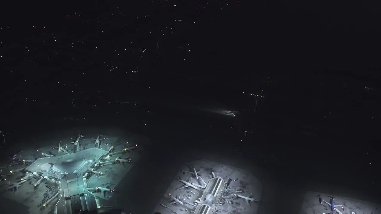 A bird's-eye-view of an airport showing several terminals with parked planes and a plane moving at night