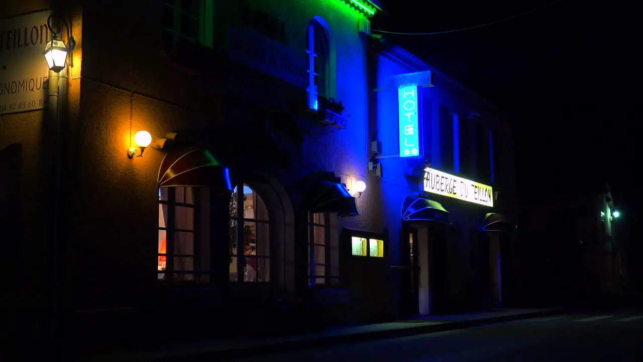 A small French hotel at night with neon sign flashing