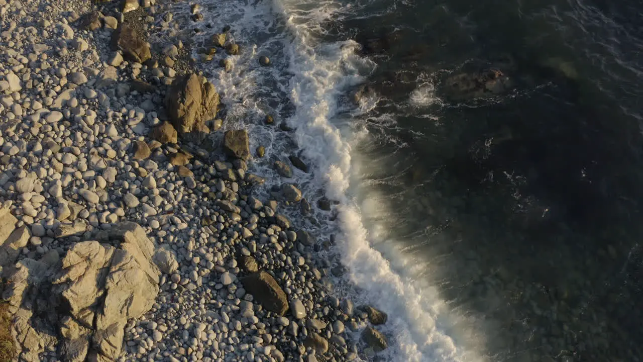 Tilt up aerial shot of Seaside coast line with big steep cliffs and beautiful inclined fields with high grass with the reveal of a ship going out of the bay on the sunset