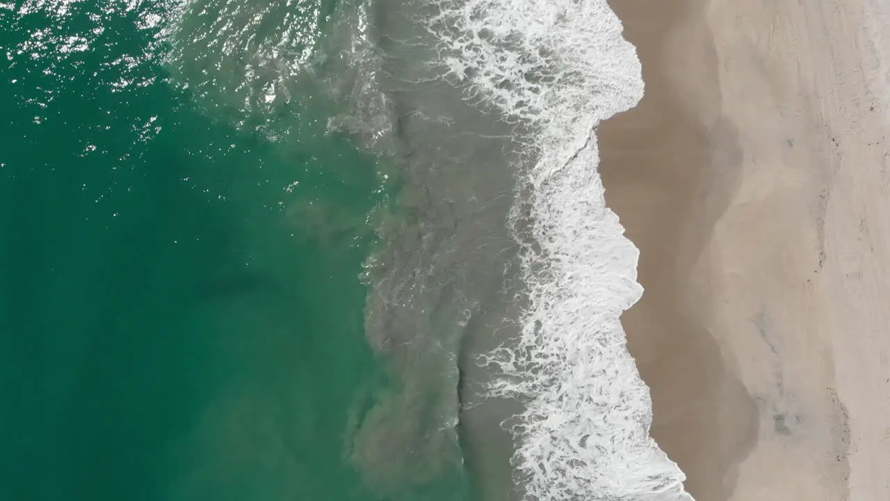 Slow aerial drone footage above tropical ocean shore with breaking waves