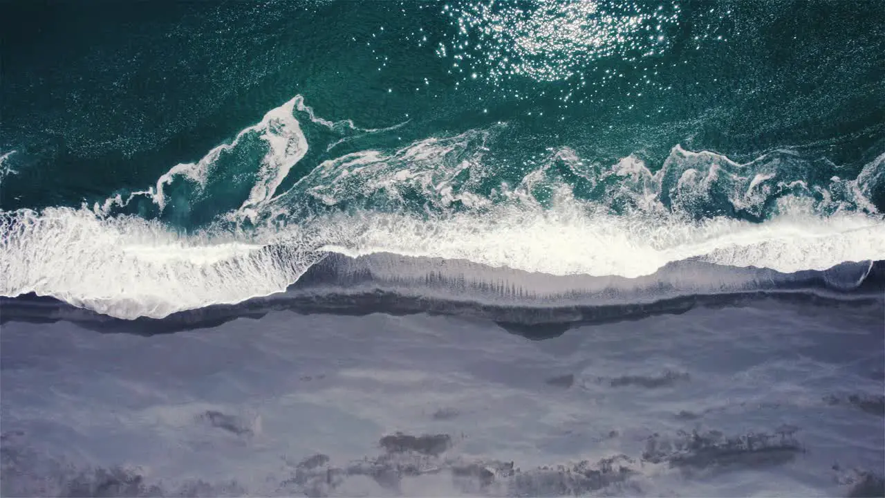 Drone shot flying sideways with camera tilted downwards above green sea and black beach in Iceland 4k