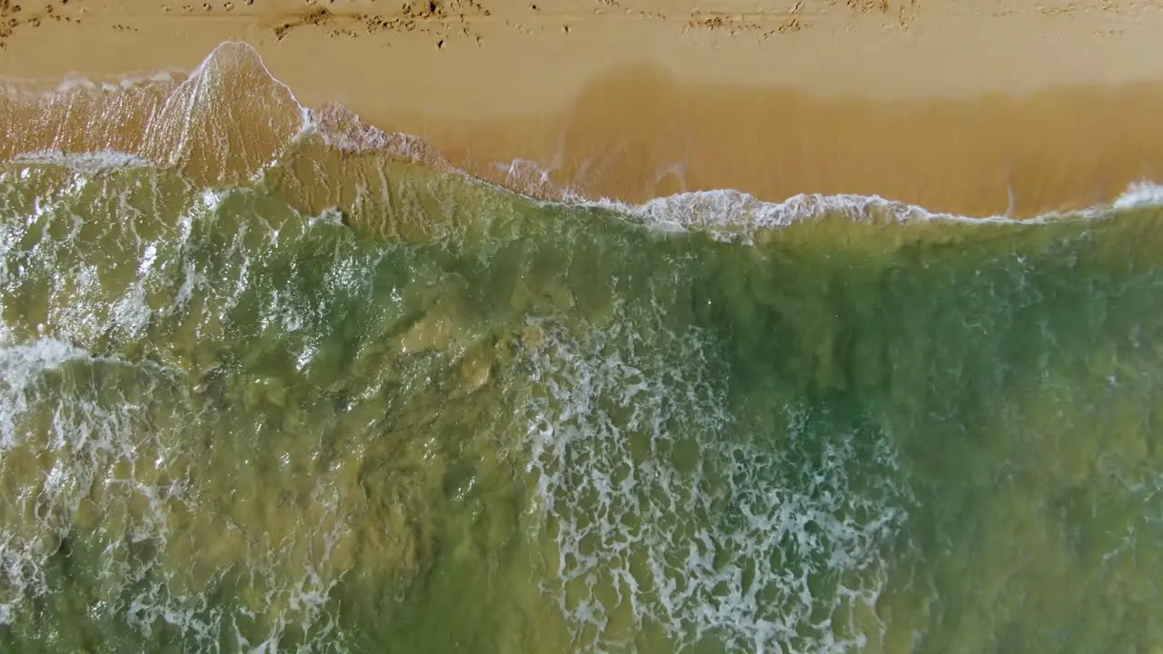 birds eye view drone descending down onto ocean waves crashing on sandy hawaiian beach