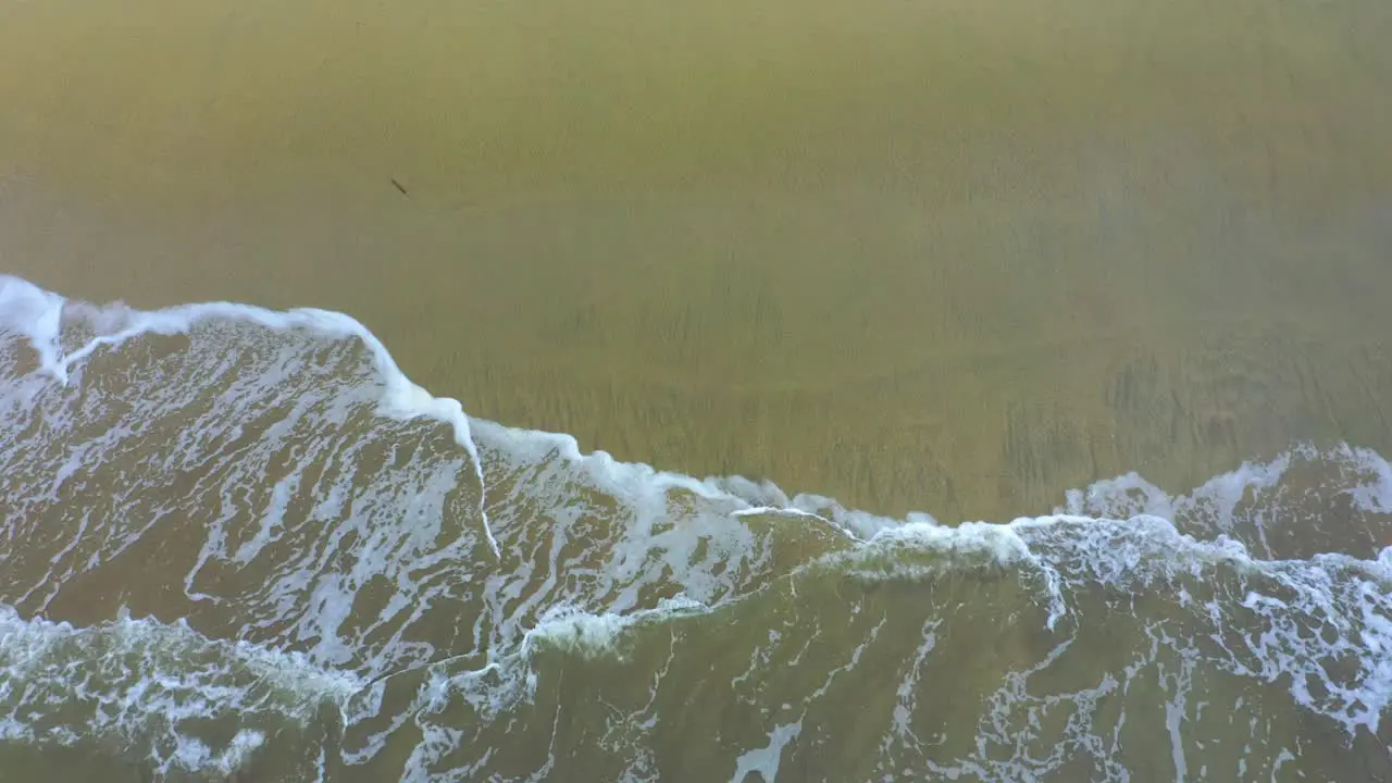 A view from the top captures little waves crashing on the beach showcasing the beauty and power of the ocean