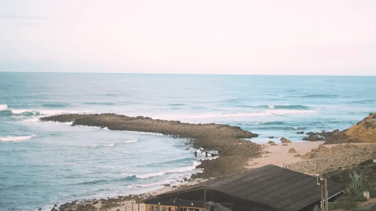 Surfers walking out to waves along shoreline Wide Shot