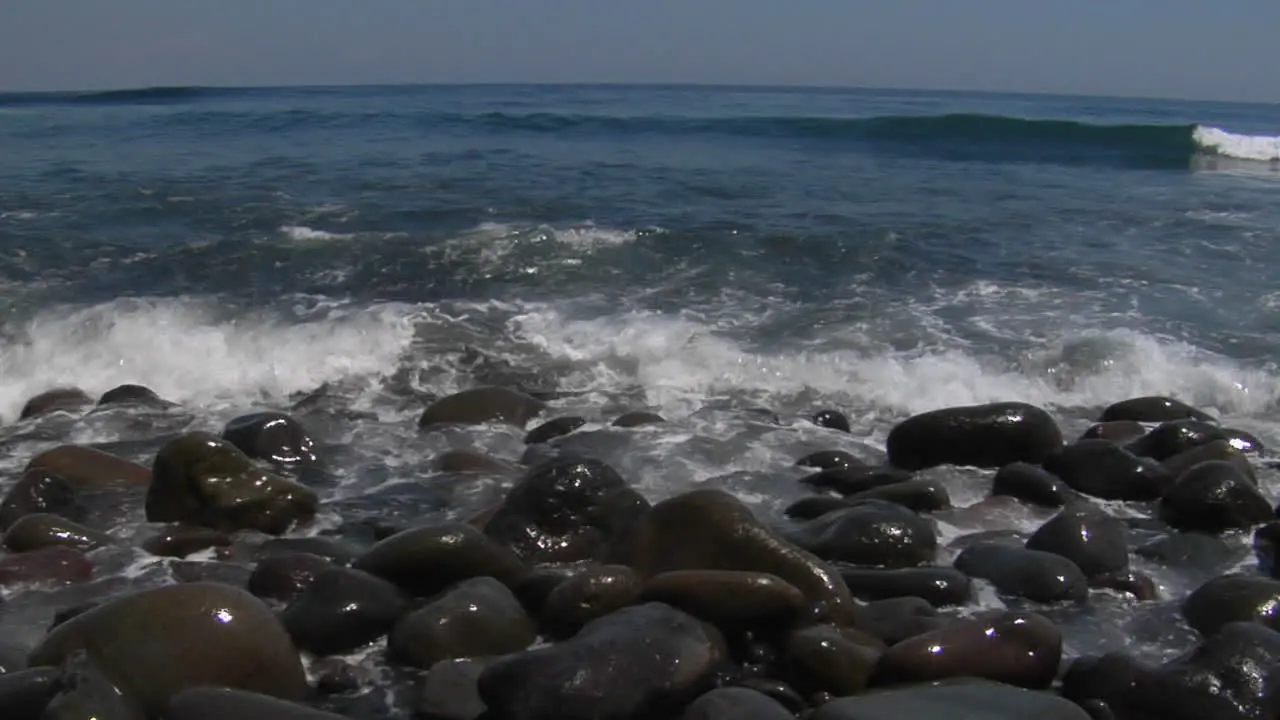 Waves Washing Over Small Smooth Rocks On The Beach