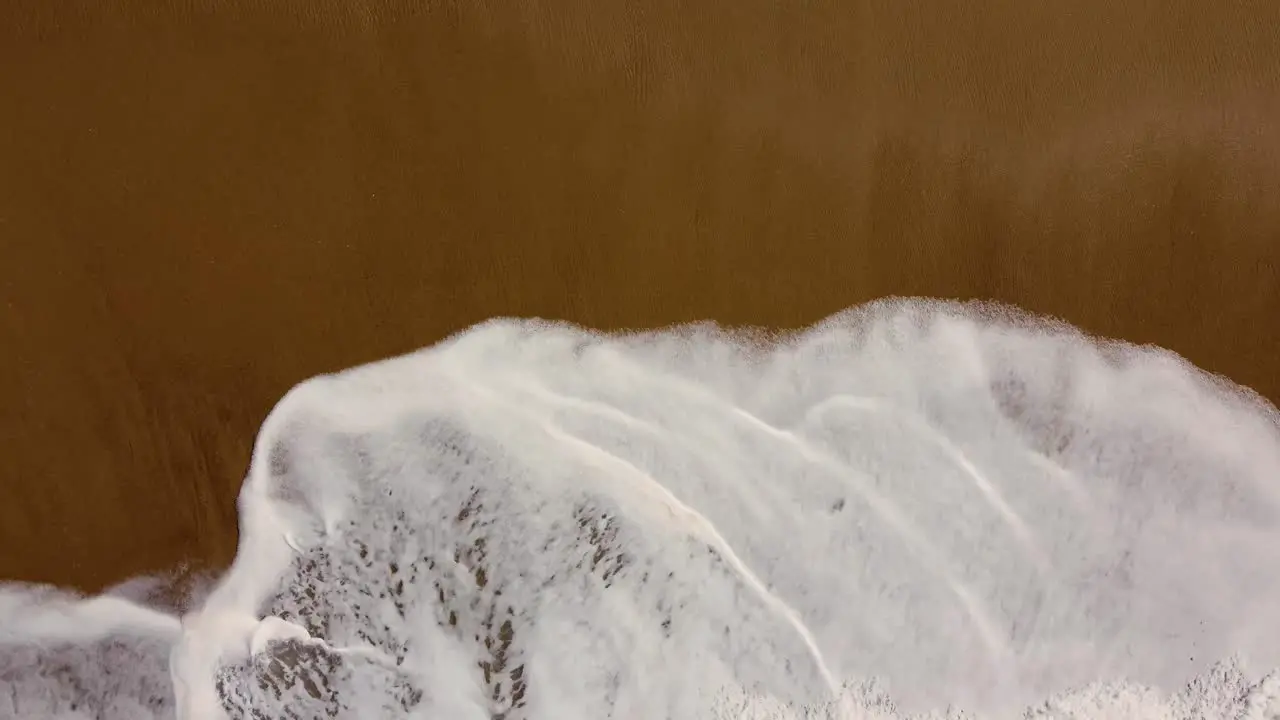 Drone aerial close-up shot of ocean water splashing up onto sandy beach beautiful Central Coast NSW Australia 4K