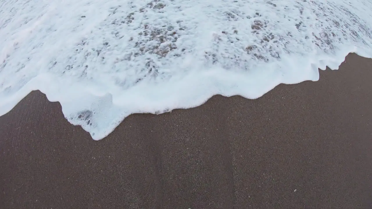 Surf rushing in and splashing over man's feet in the sand