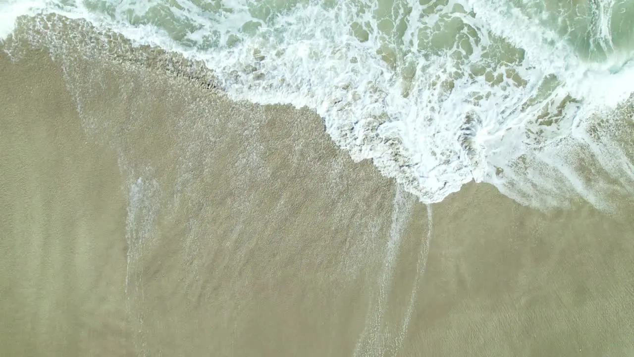 Close up straight down drone shot of waves crashing over the brown sand on Hutchinson Island in South Florida